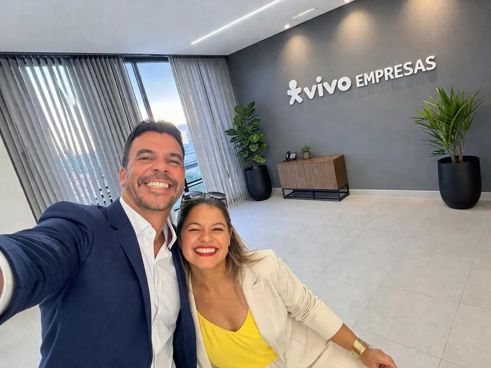 Duas pessoas da equipe da Connect4Me sorrindo para a foto no lobby, com a logomarca Vivo Empresas na parede ao fundo